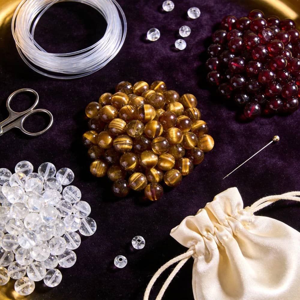 Metal element DIY bracelet making kit with loose Clear Quartz, Tiger Eye and Garnet beads, cord and tools on dark velvet